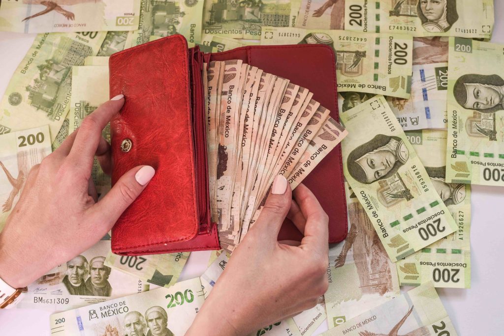 Mujer con billetera roja sacando pesos mexicanos porque tiene una buena estabilidad economica