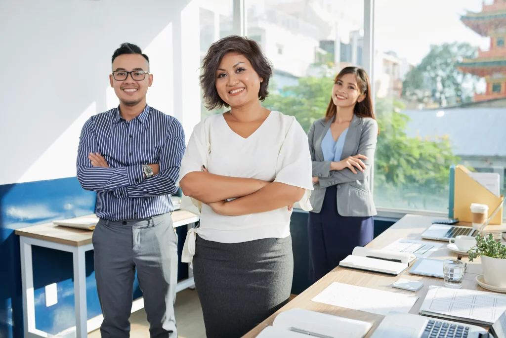 Dos mujeres y un hombre en trajes formales posando en una oficina.