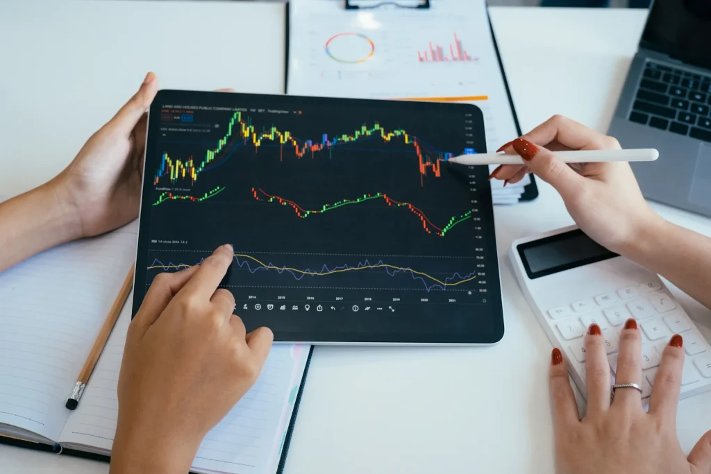Personas revisando gráficos de inversión en una tableta y tomando notas, representando la importancia de la educación financiera para aprender sobre inflación, retorno y diversificación antes de invertir.