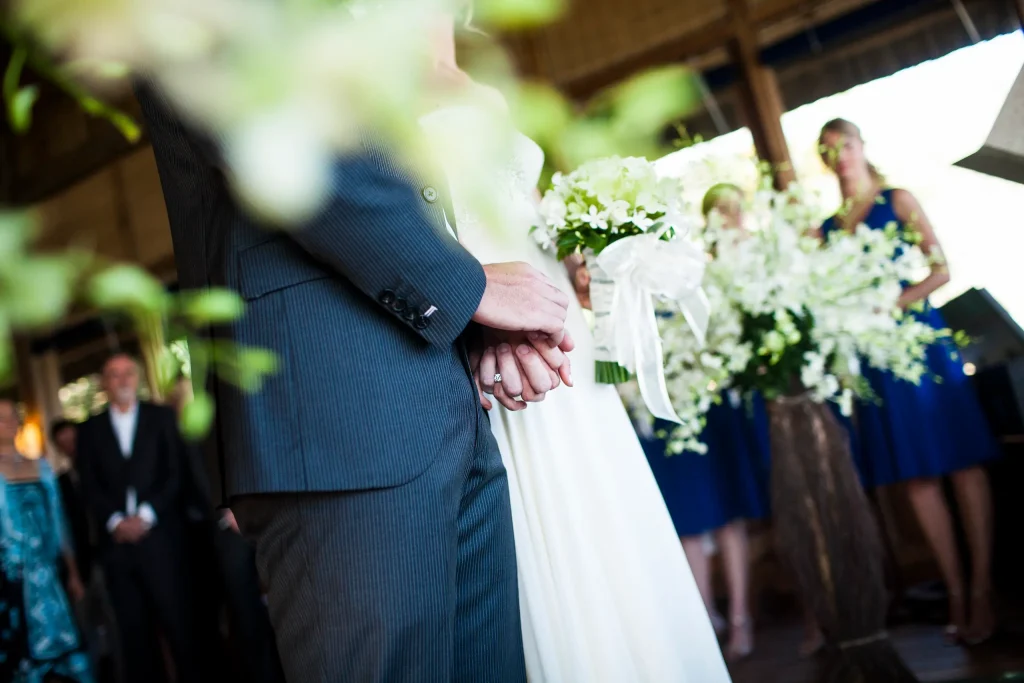 Pareja tomada de la mano durante una boda con invitados al fondo.